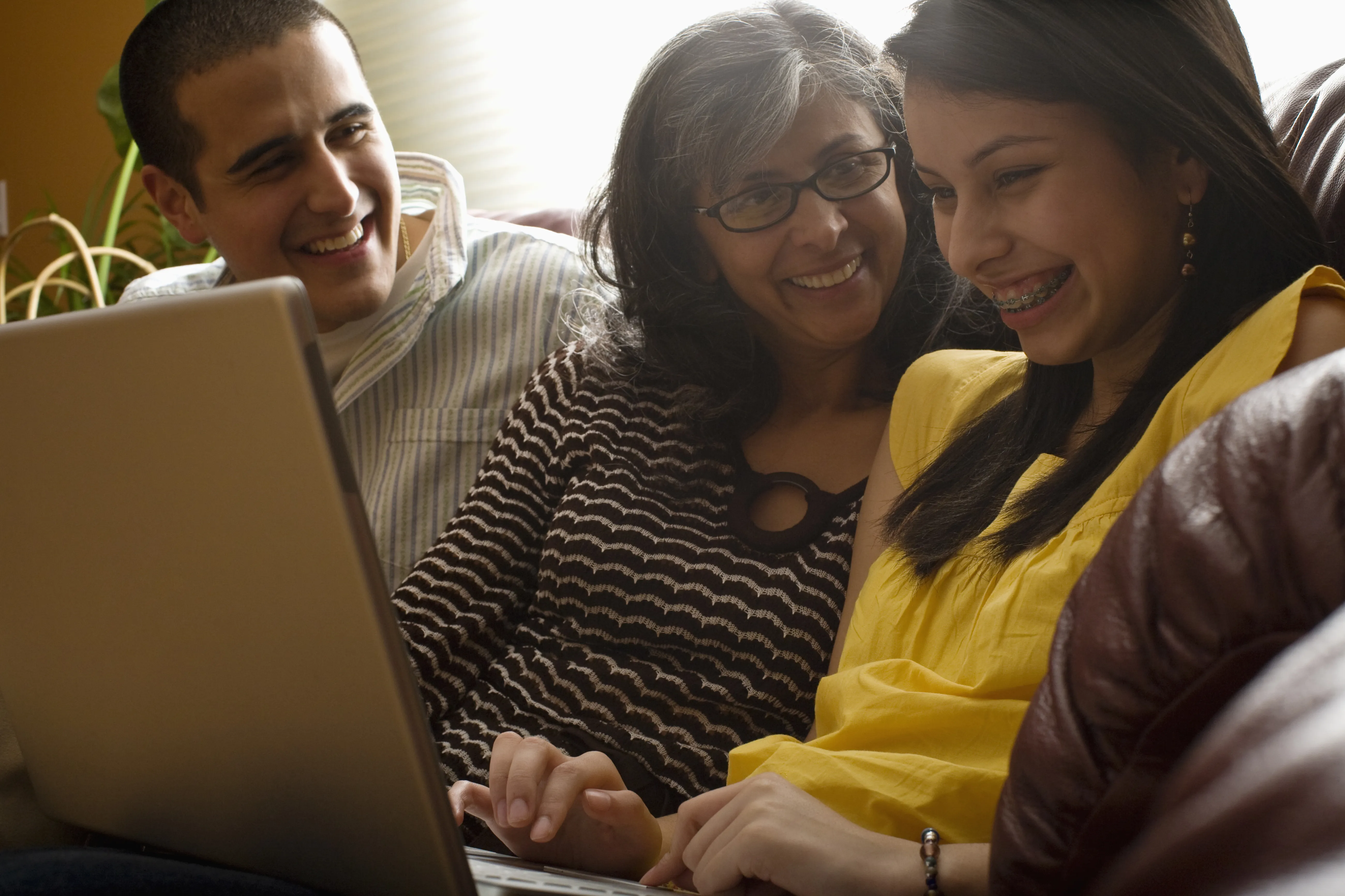 A mother sitting in the middle of her son and daughter with a laptop laughing. 