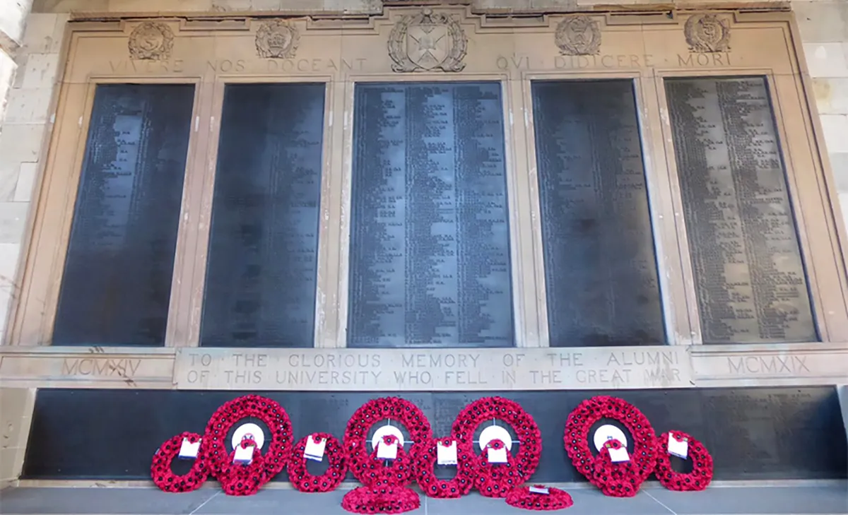 Memorial wall at Old College with multiple poppy wreaths laid in front of it.