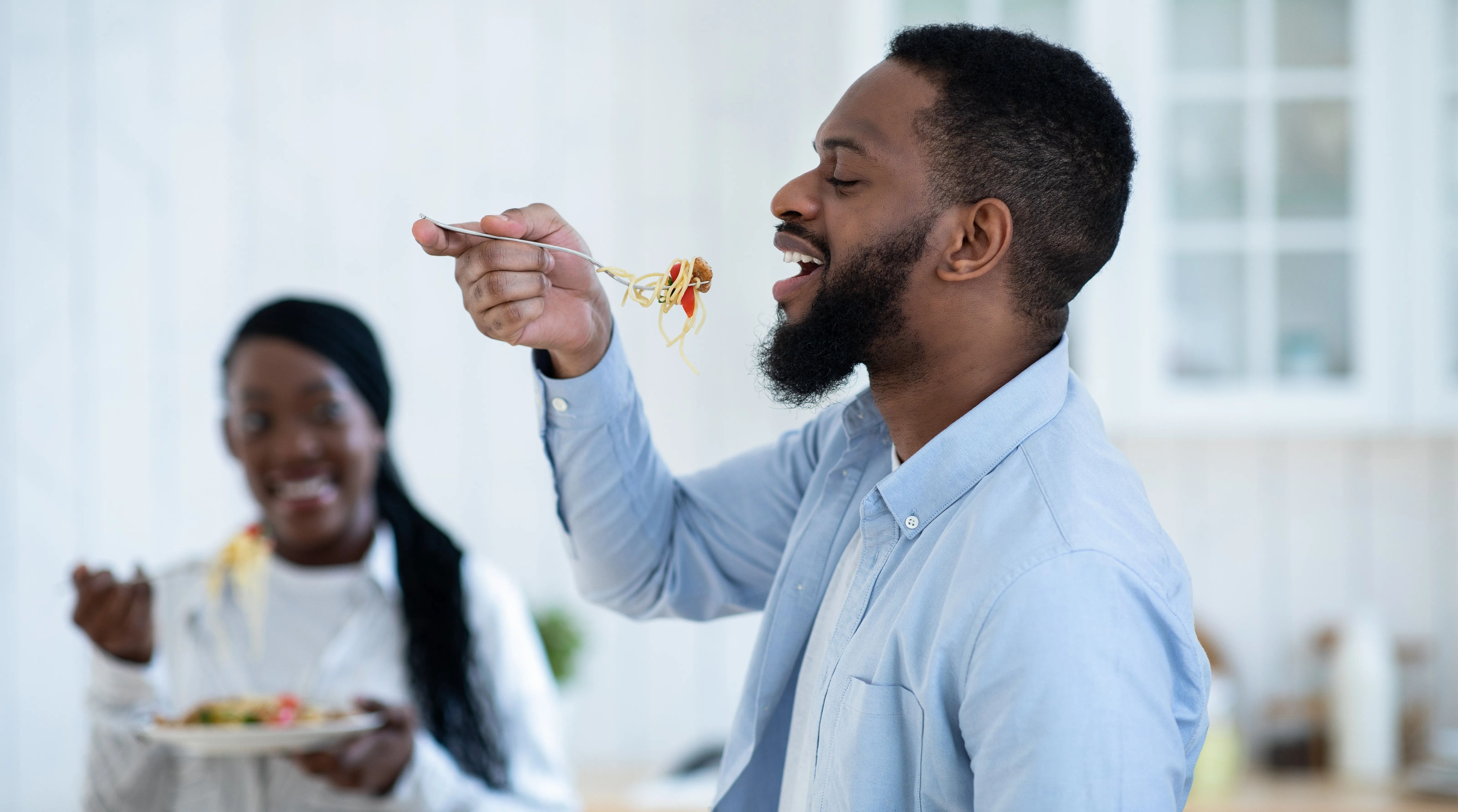 Man tasting spaghetti while having lunch with wife in kitchen