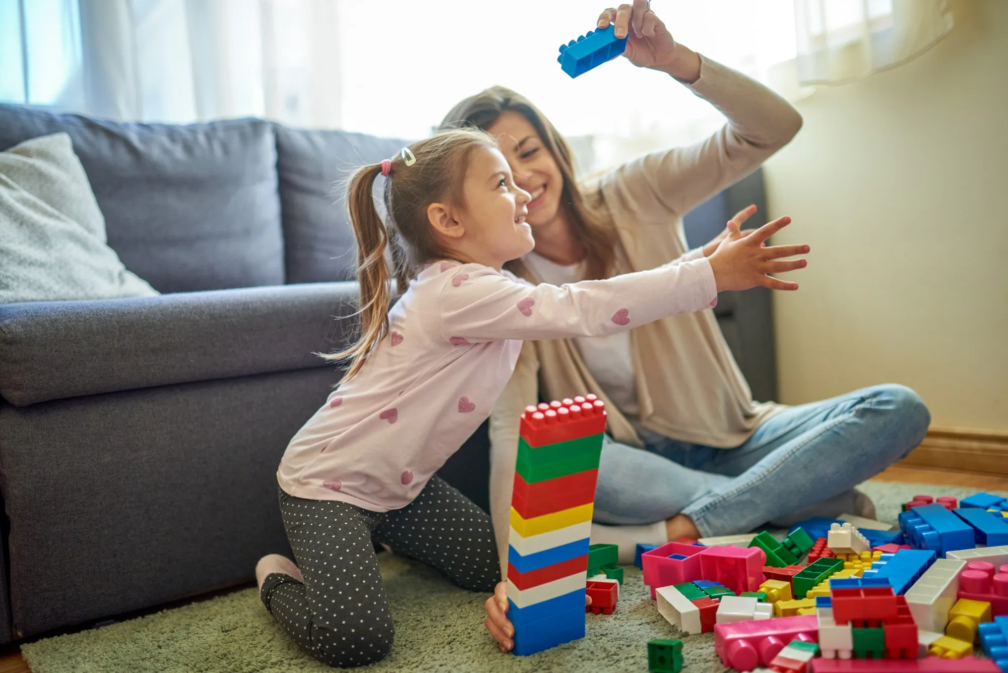 Mother and daughter sat on living room floor playing with coloured cubes