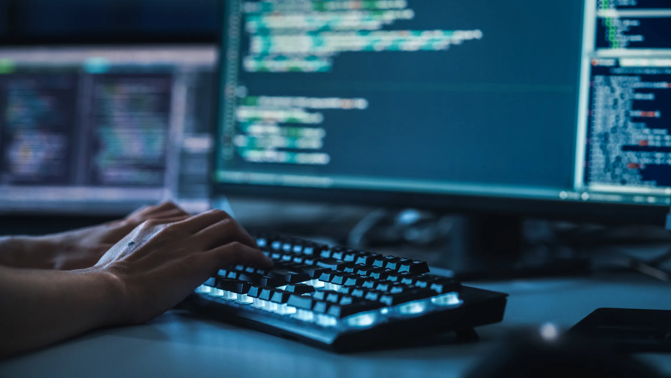Close-up image of person's hands typing in front of blurred computer screens
