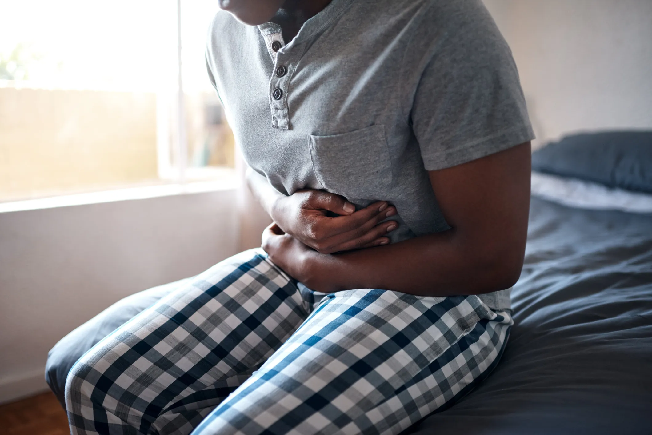 A photograph of a man sits on the edge of his bed clutching his stomach in pain