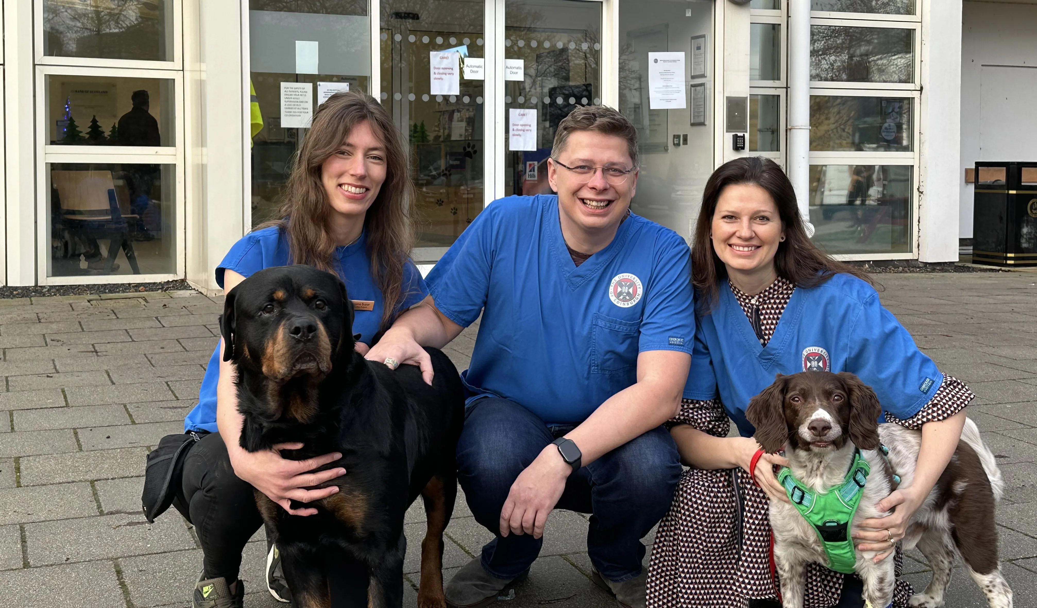 K9-LiquiDX team pictured kneeling on floor outside vet clinic with two dogs