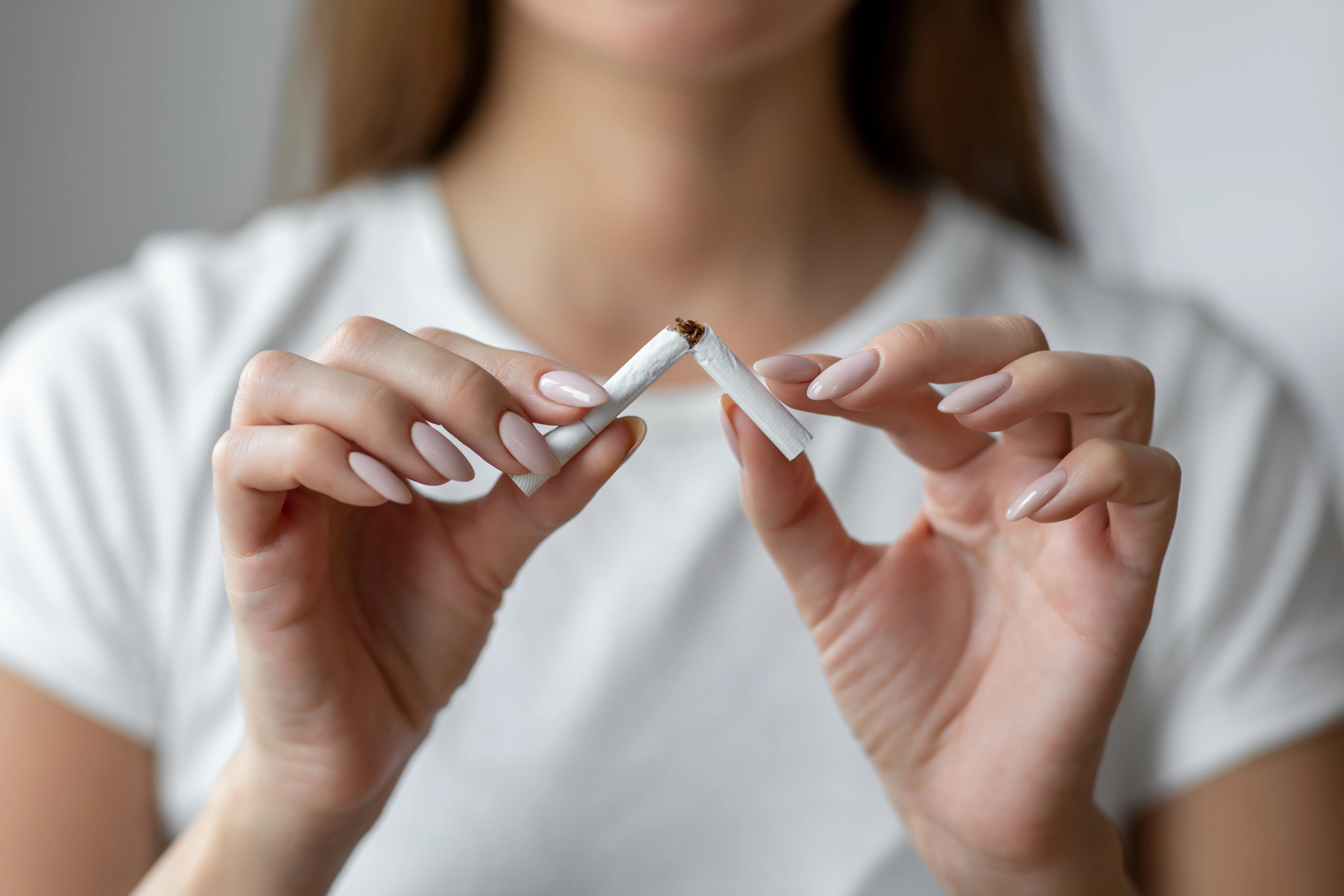 A photograph of a woman holding and breaking a cigarette with her hands