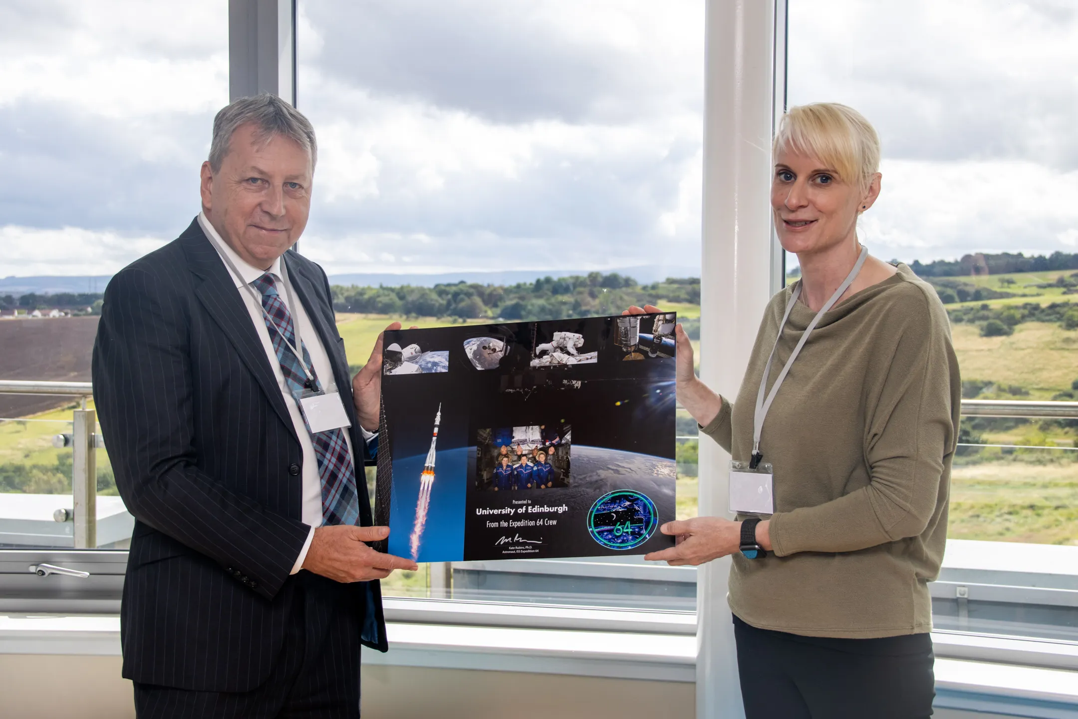 Principal Peter Mathieson stands next to astronaut Kate Rubins holding a large collection of photographs of space.