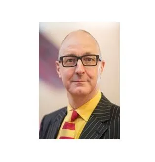 Photograph of Simon Fanshawe, head and shoulders wearing yellow shirt and red/yellow striped tie. He is wearing glasses.