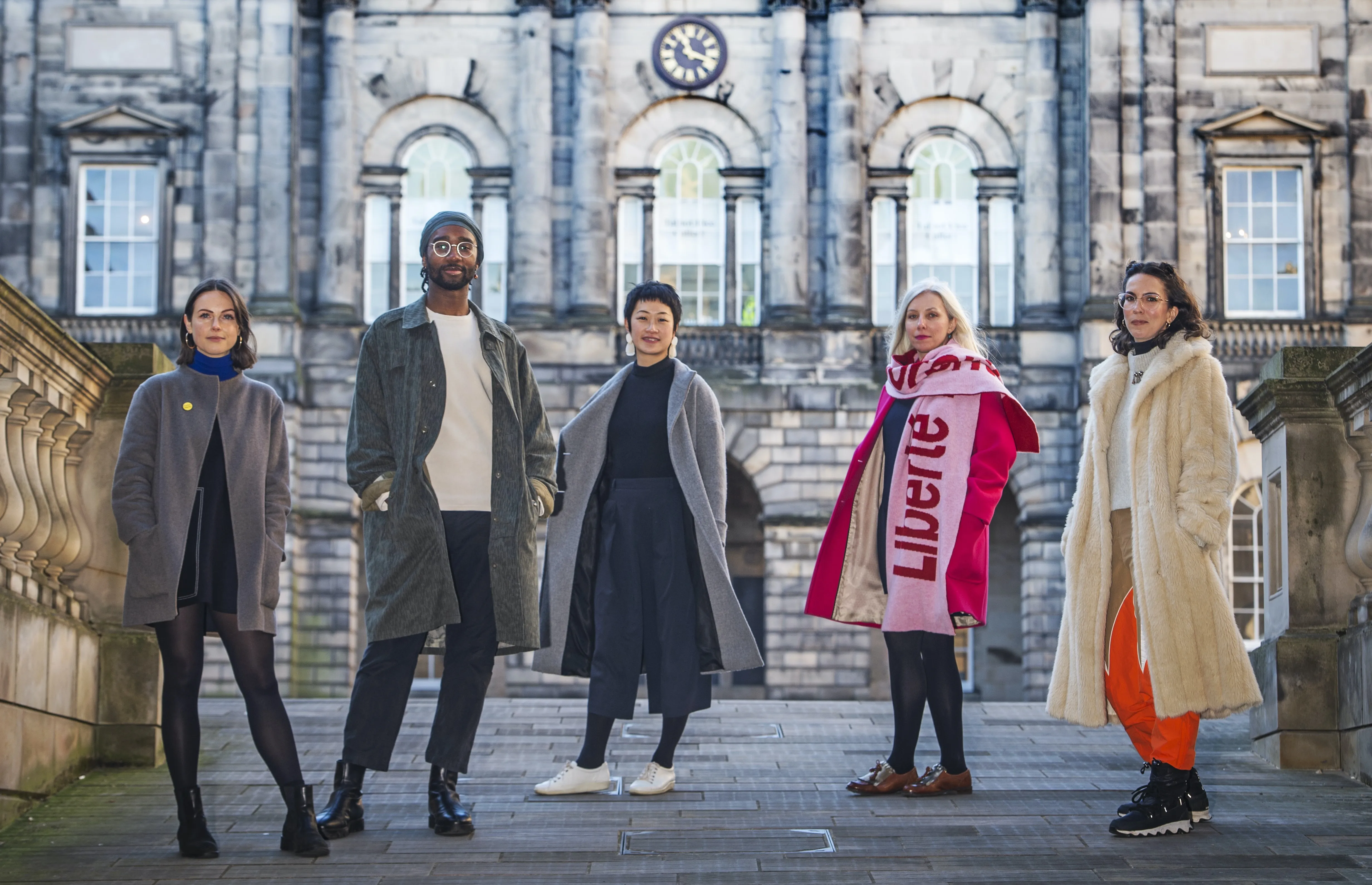 5 people stand looking to camera in front of an old building