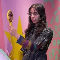 A student artist poses in front of their installation looking in a mirror. 