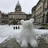 A miniature snowman in the shape of a bear sits on a stone handrail in Old College Quad