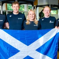 A group of swimmers from the University stand in a group holding a Scottish flag