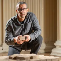 Artist Taysir Batniji pictured kneeling beside his sculpture, which is made from stacked bars of soap sitting on a pallet. 