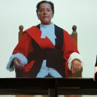 Artist Carey Young pictured sitting in front of a still frame featuring the image of a female judge, from her film ‘Appearance’.
