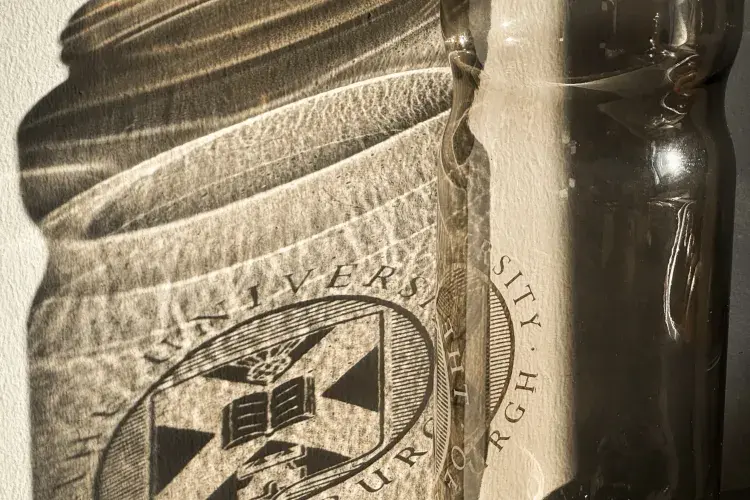 Hard light shining through a branded Uniersity of Edinburgh bottle creates a shadow with an outline of the logo on a nearby wall