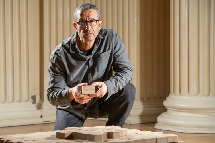 Artist Taysir Batniji pictured kneeling beside his sculpture, which is made from stacked bars of soap sitting on a pallet. 