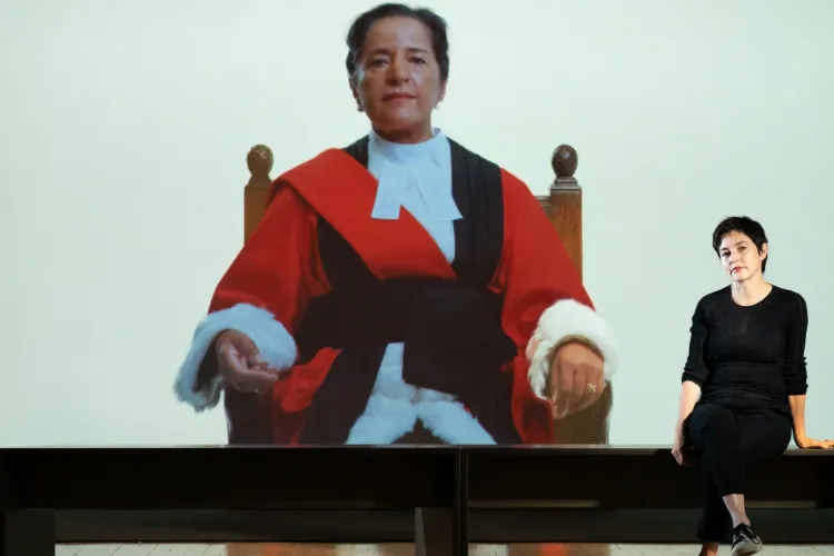 Artist Carey Young pictured sitting in front of a still frame featuring the image of a female judge, from her film ‘Appearance’.