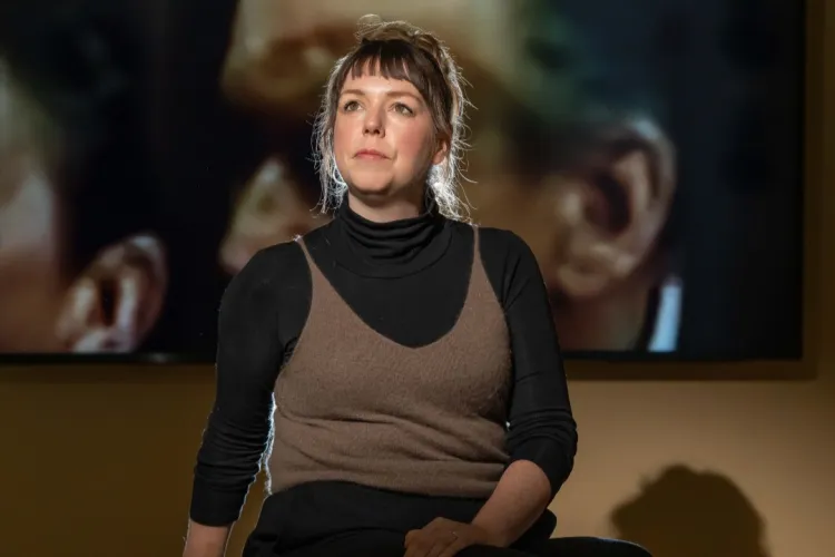 Filmmaker Jenny Brady pictured sitting in front of a blurred still featuring two people from her film The Glass Booth. 