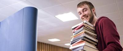 Student in library carrying a large stack of books
