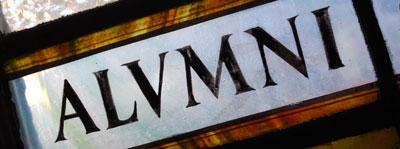 Stained glass of the word "alumni" in capitals, with the 'u' written as a 'v'