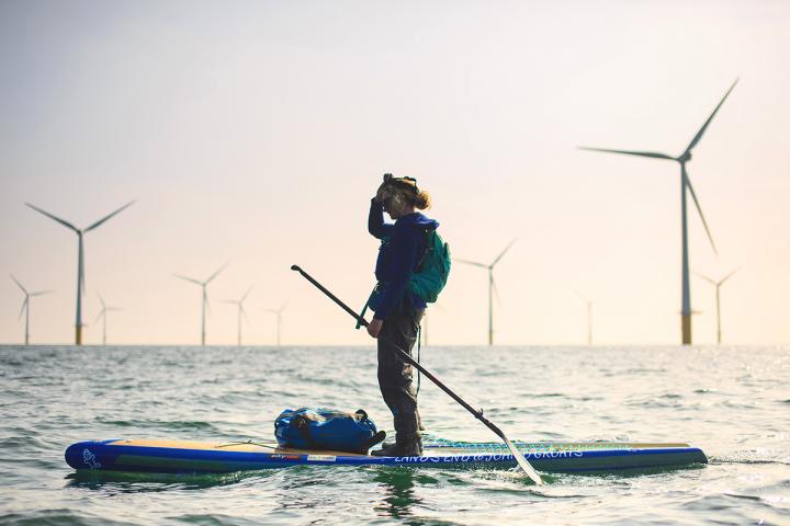 Cal on her paddleboard with wind turbines on the horizon
