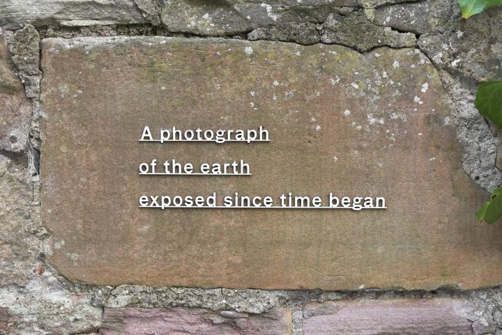 a text cut in stainless steel reading 'A photograph of the earth exposed since time began and installed on a stone wall