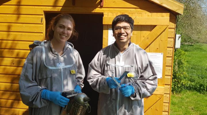Students Abigail and Ani, wearing bee suits, stand outside a shed at the Easter Bush Campus Apiary.