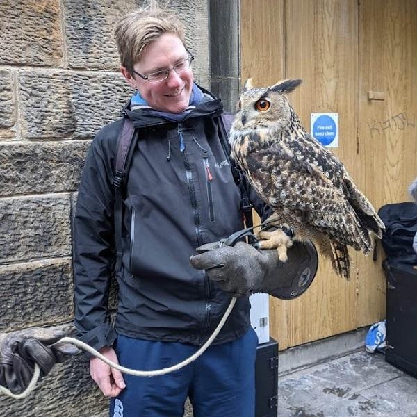 A photo of Andre holding a large eurasian eagle owl on his left arm. he is looking at the owl and smiling.