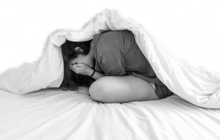 A black and white photo of a woman hiding underneath a duvet.