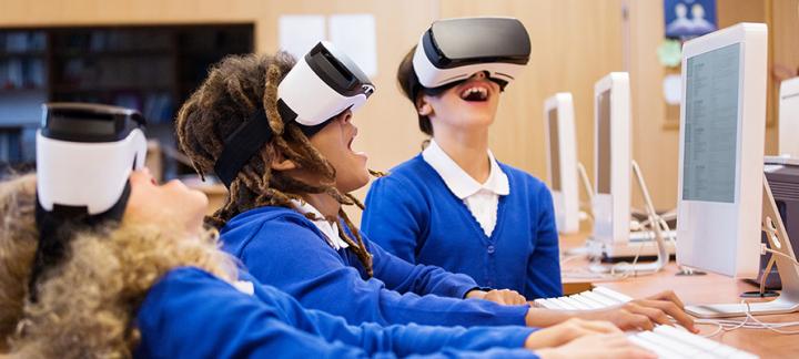Three school pupils wearing augmented reality goggles at their PCs