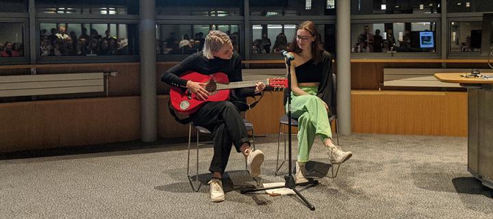 Photo of two students singing and playing the guitar