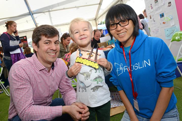 Adult and child with Roslin Institute reseracher showing off their papercraft model of skin and its structure.