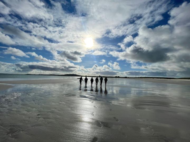 Six people standing on the beach backlit by the sun