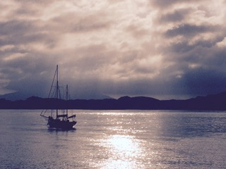 Photograph of a boat on water, hills in the distance and overhead a cloudy sky