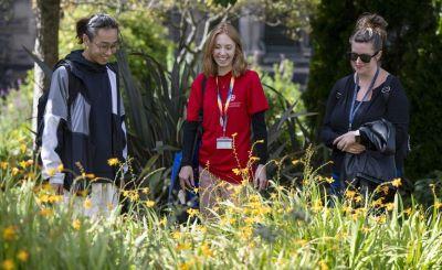 University staff and students smile at bright yellow flowers growing on campus