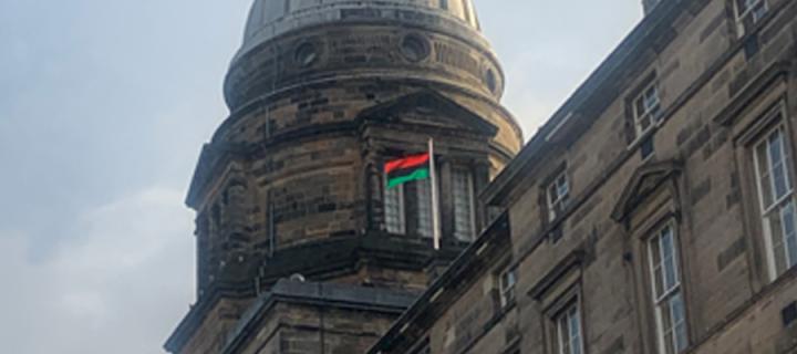 A red, green and black striped flag, flying on the roof of the University building, Old College