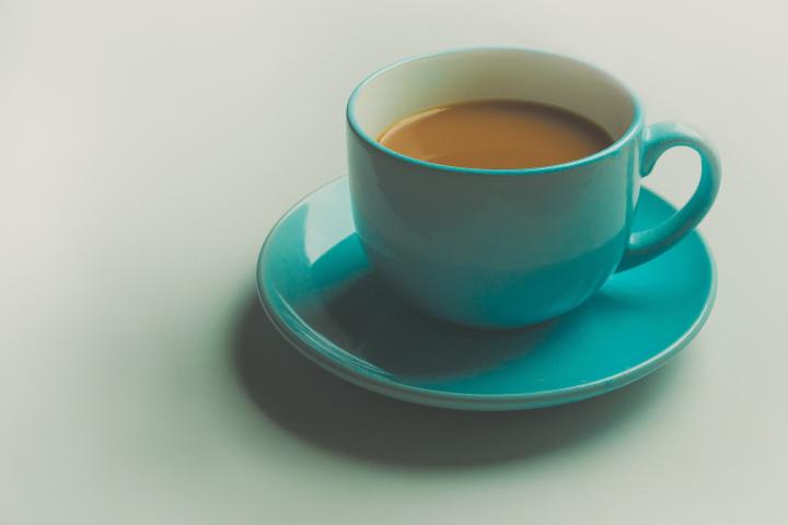 Photograph of a cup of tea in a blue cup on a blue saucer. The teacup is surrounded by a white background. 