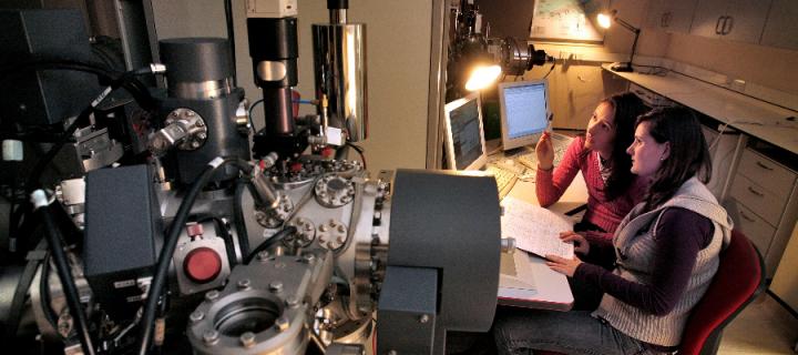 Two female scientists seated looking at computer monitors and surrounded by scientific equipment