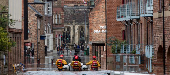 Rescuers with a boat and wading through the water of a flooded street in the middle of York city buildings