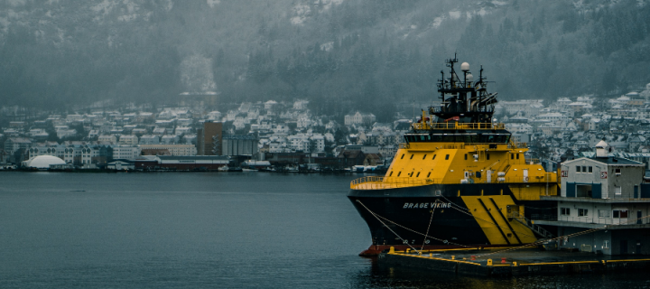 Yellow and black boat docked at Bergen, Norway with snowy town in backdrop