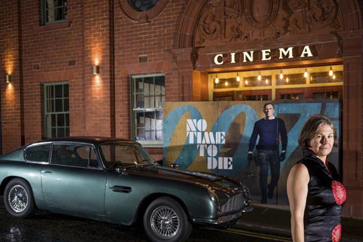 Photo of Carol standing outside her cinema with a car and film poster