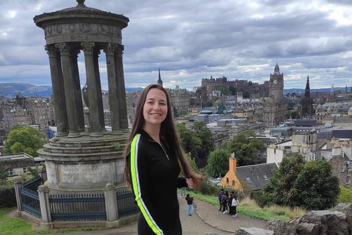 Photo of Celeste Callen on top of Calton Hill with the Edinburgh skyline behind her