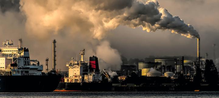 Image of ships at a port, with a factory in the background emitting plumes of smoke