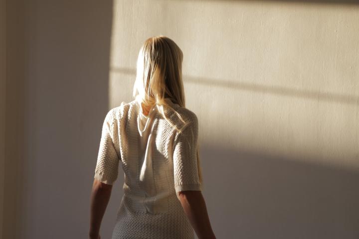 A woman looking toward a wall with her back facing the camera.