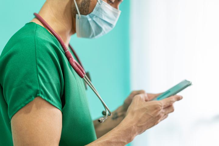 A male member of clinical staff in scrubs uses his mobile phone