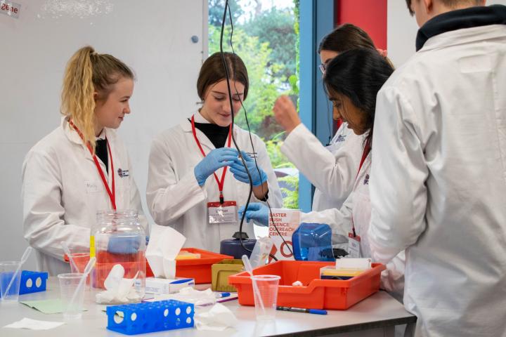 A PhD student teaches school pupils how to use lab techniques.