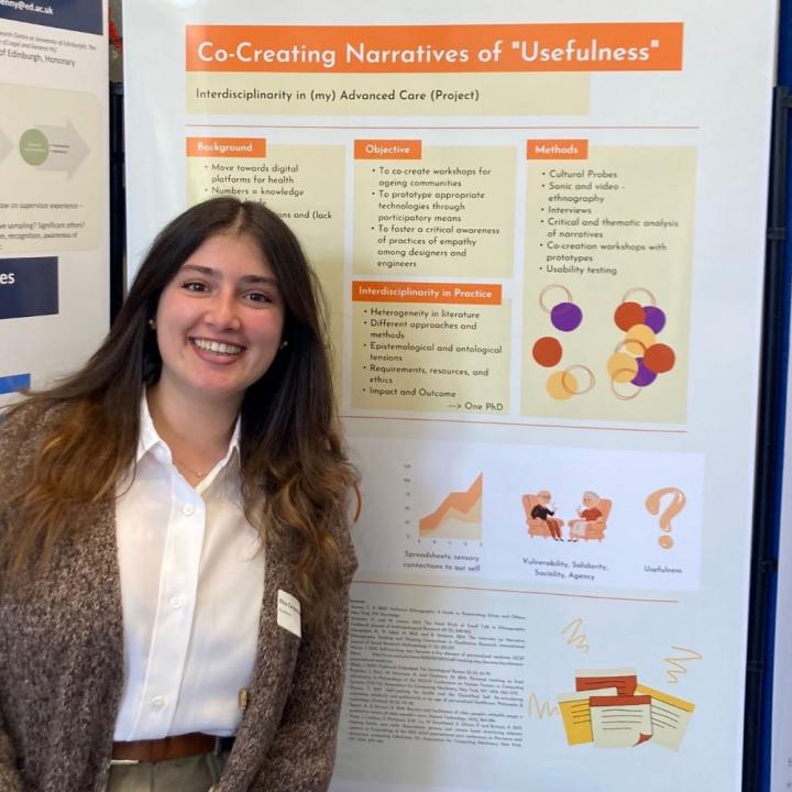A smiling young woman with long brown hair stands in front of a research poster.