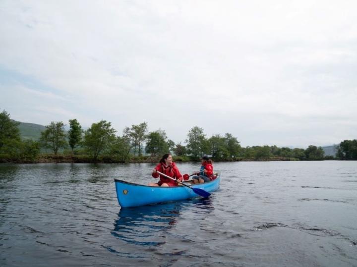 Two young people are in a canoe on a wide lake. The overhead sky is grey.