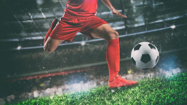 Close up of a soccer scene at night match with player in a red uniform kicking the ball with power - stock photo