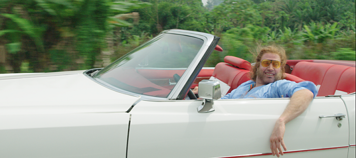 Still from a film showing a man driving an open top car