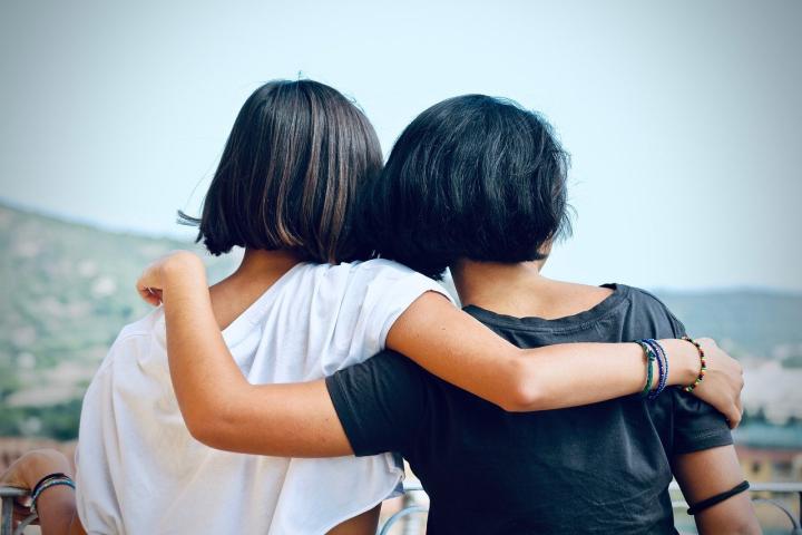 Photograph of two women with an arm around one another. They both have there backs to the camera.