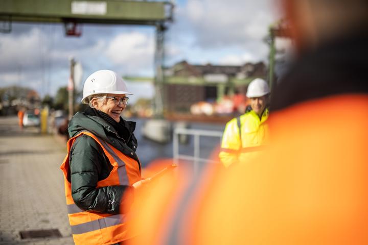 A worker in a hard hat and high vis vest laughs at two other works in high vis vests who are out of focus in the shot
